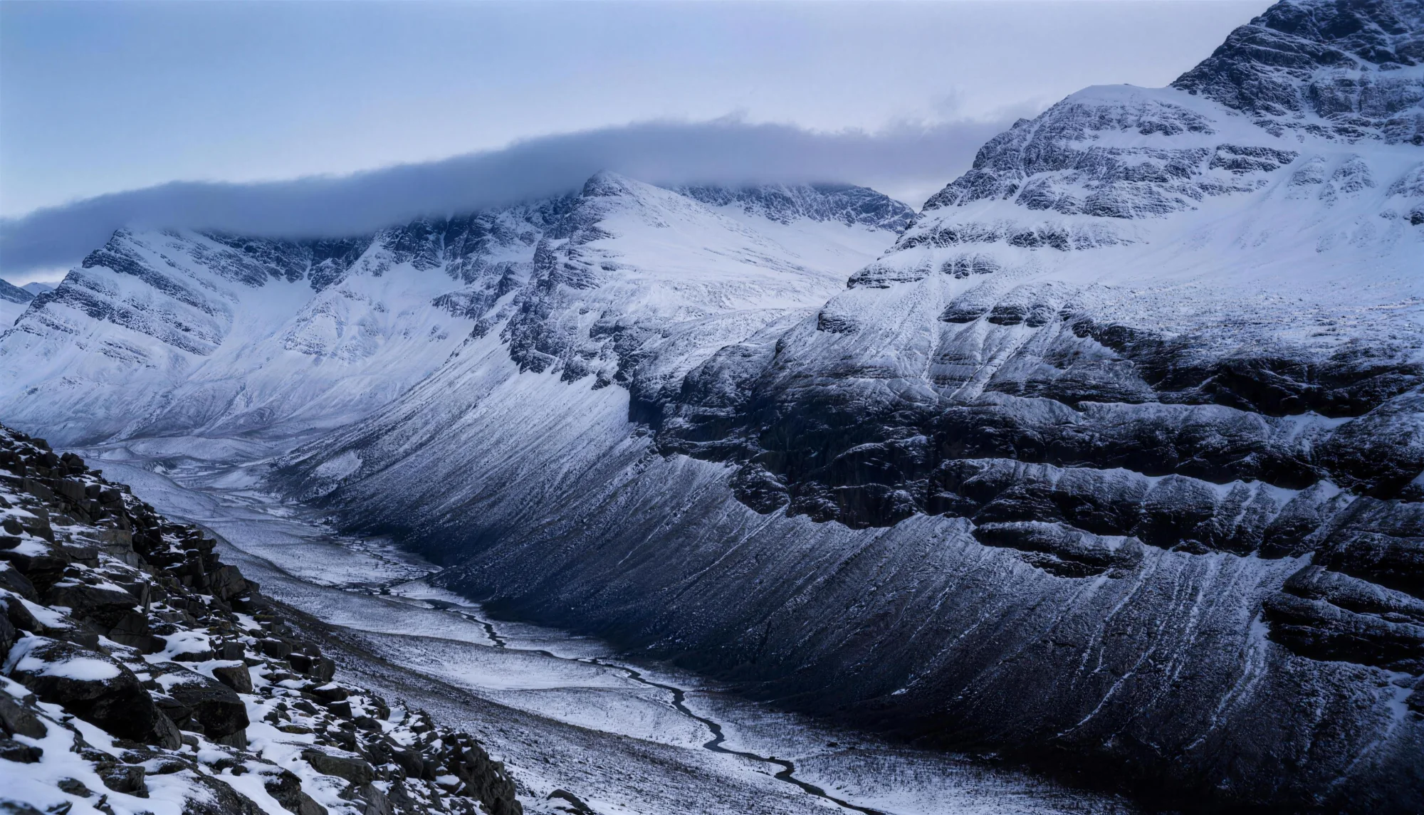 Snow covered peaks above a dark rocky corrie, cloud sitting flat across the tops.